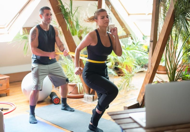 A couple working out on yoga mats indoors, using a laptop for guidance.